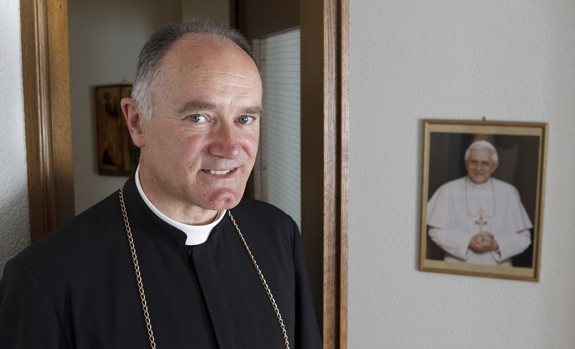 Bispo Fellay ao lado de um quadro do apóstata Bento XVI.